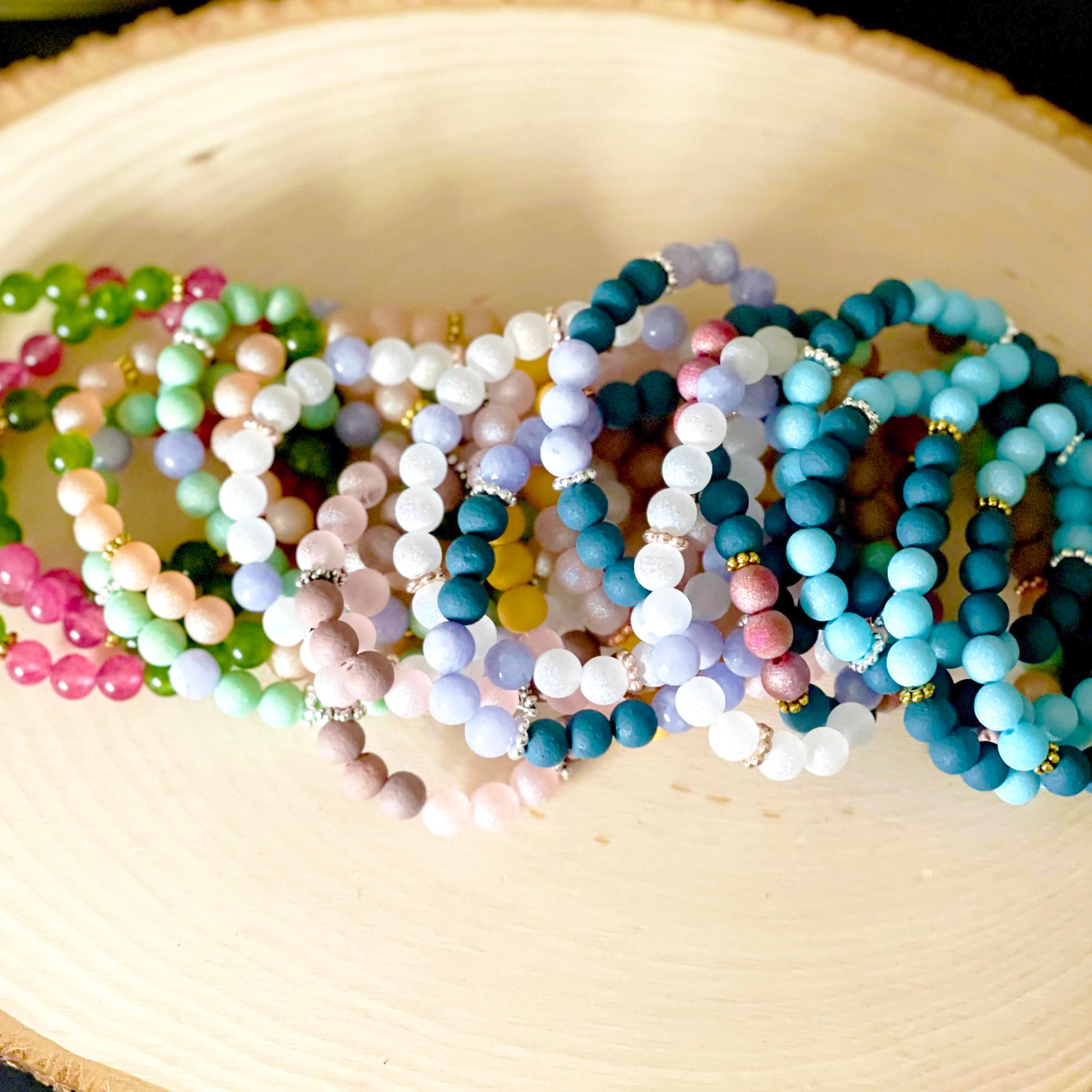 Multiple bracelets made of multi-color glass beads and metal spacers, laying on a wood backdrop