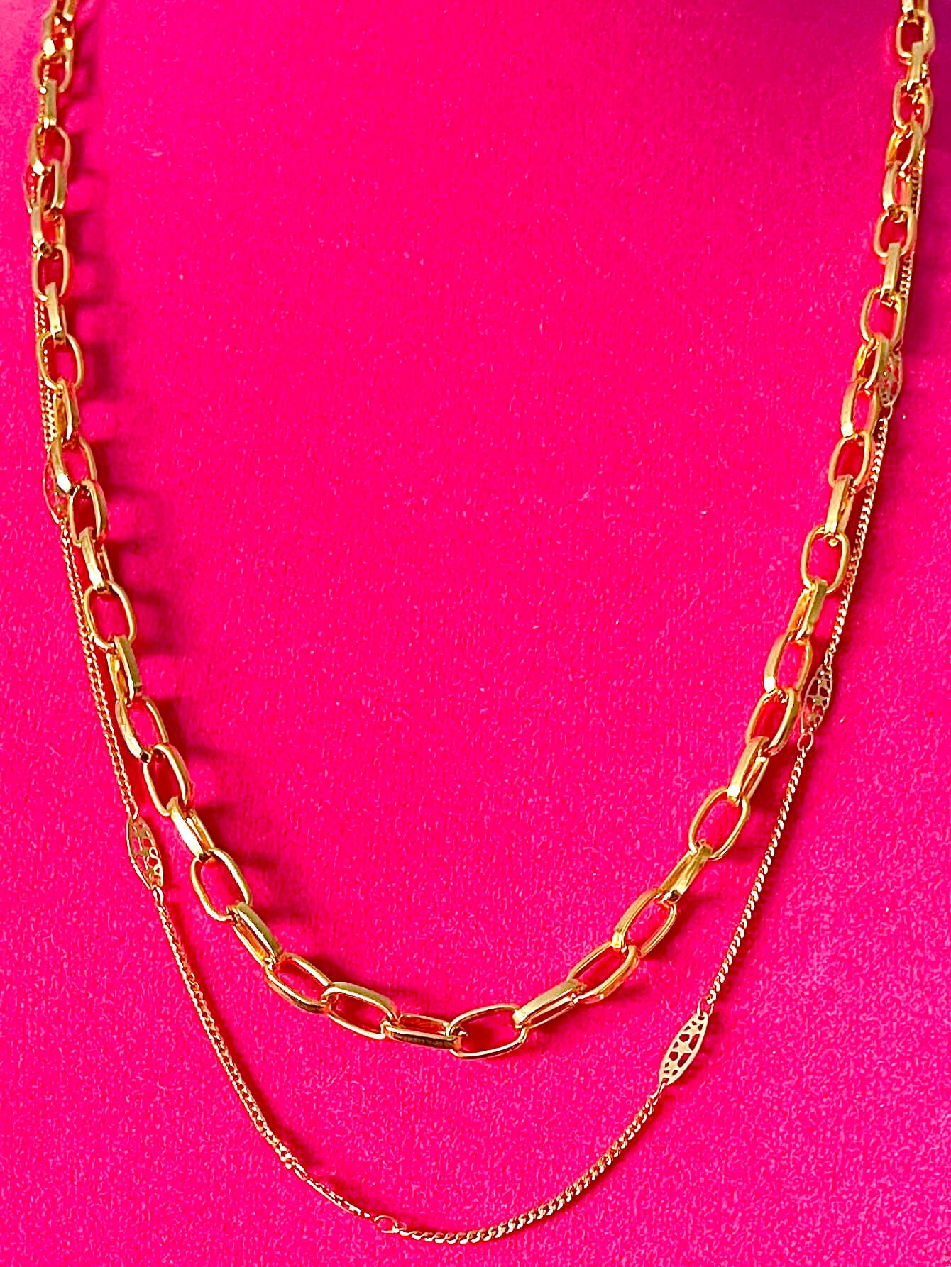 Yellow brass chain necklaces on a pink backdrop