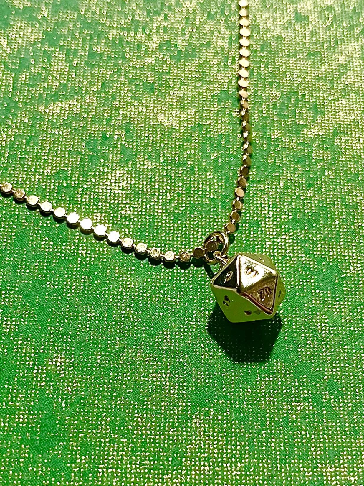 Gold plated polyhedral charm on dot necklace chain with green background