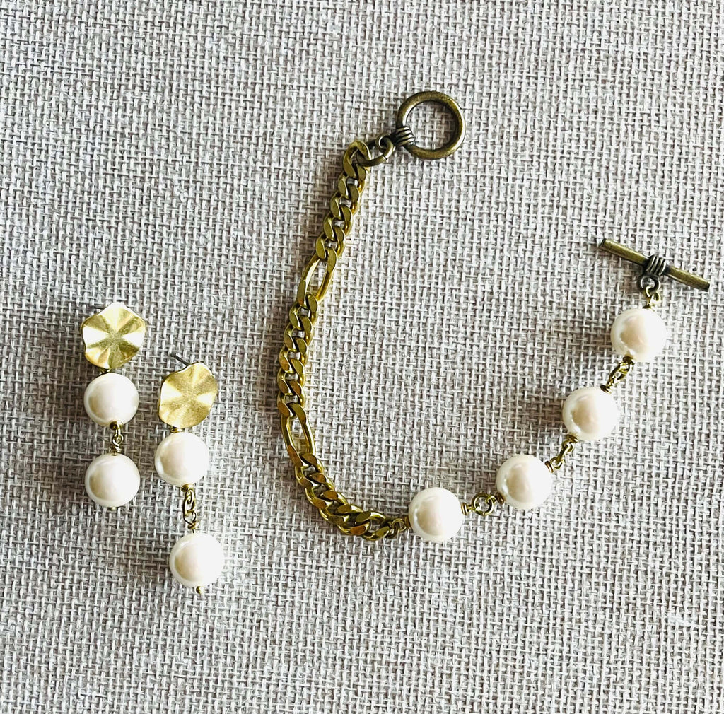 Yellow brass bracelet and earrings with white pearls on tan background 