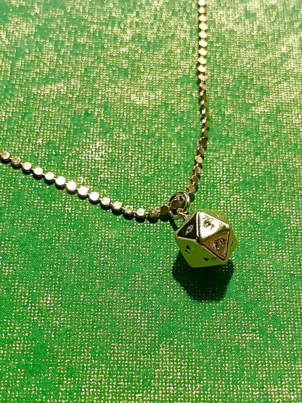 Gold plated polyhedral charm on dot necklace chain with green background