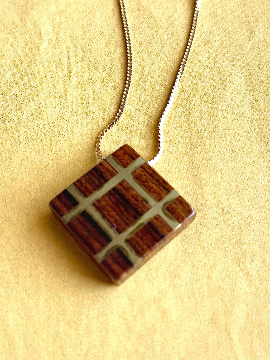 Square wood pendant with yellow brass grid inlay on yellow brass chain with yellow background